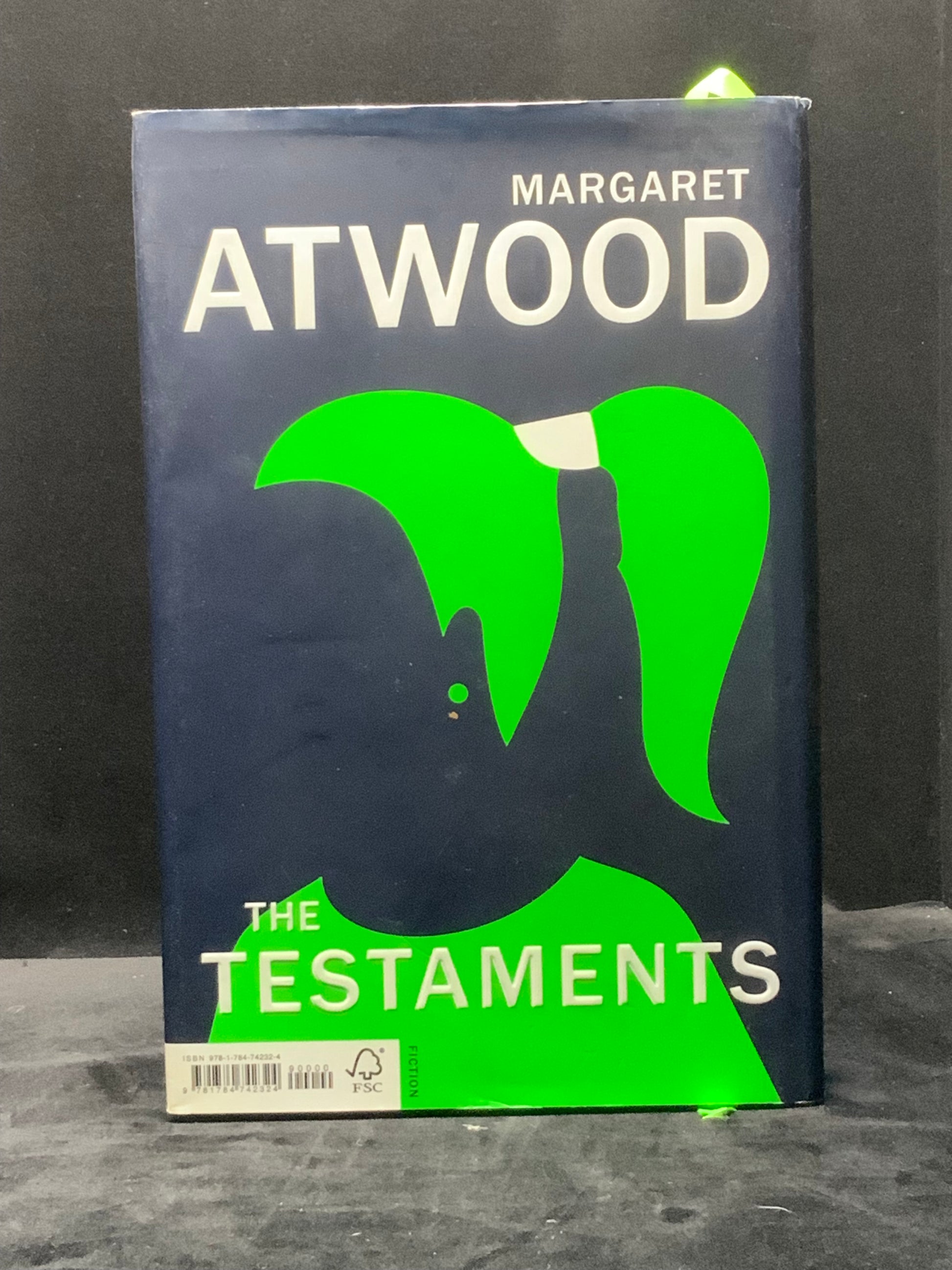 Book titled 'The Testaments' by Margaret Atwood with a green and black cover on a dark surface.