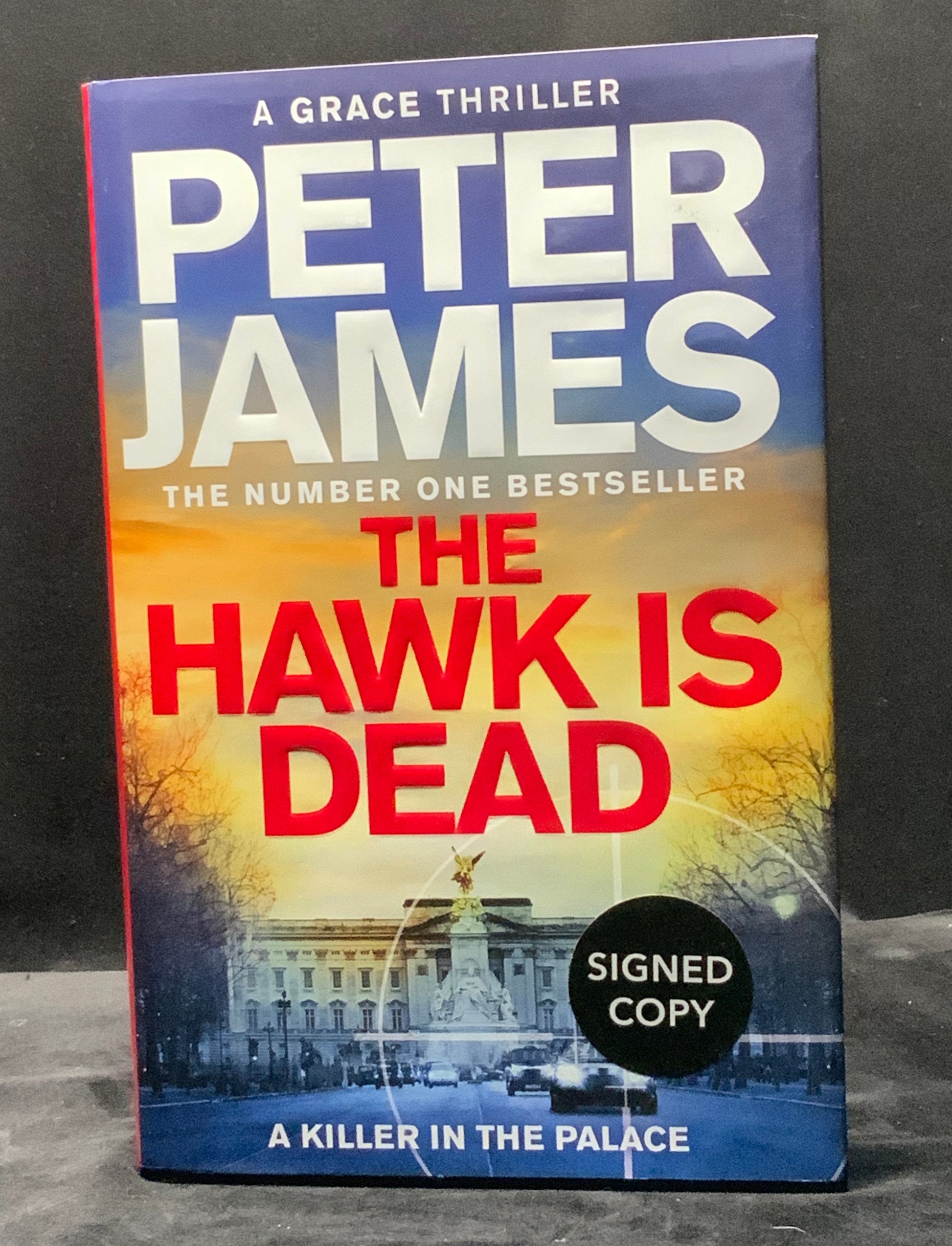 Book titled 'The Hawk is Dead' by Peter James with a signed copy label on a dark background